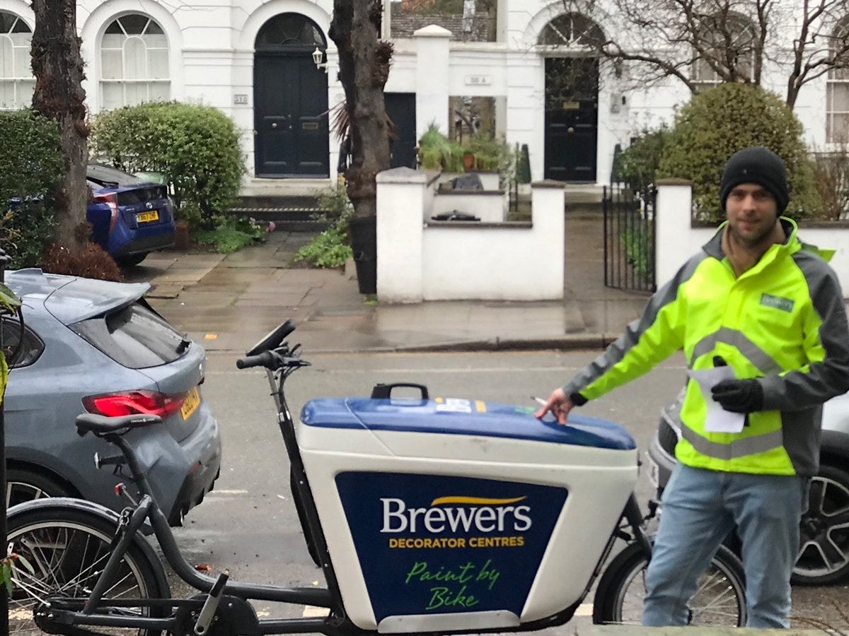 A delivery rider arrives at the destination on a residential London street. The cargobike is branded with the paint supplies company he is working for. A delivery rider arrives at the destination on a residential London street. The cargobike is branded with the paint supplies company he is working for.