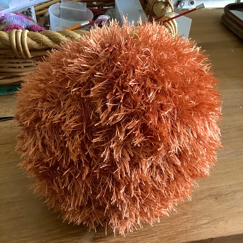 Orange fluffy fur being knitted up into two round shapes.