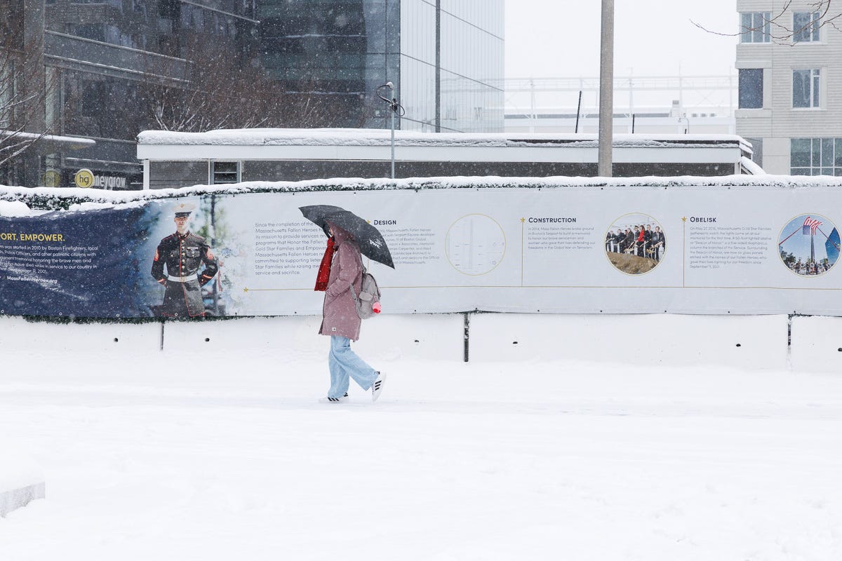 Pedestrian walking with an umbrella in heavy snowfall beside a mural-covered construction wall in Boston.