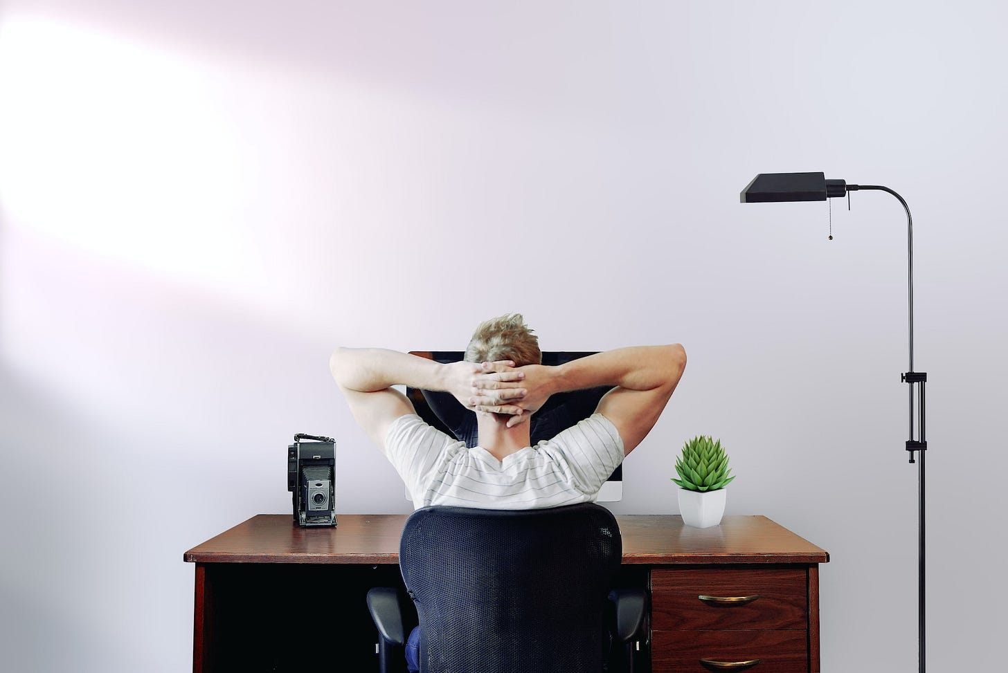 A young man looking at monitor with hands at the back of the head A young man looking at monitor with hands at the back of the head