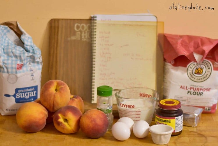 Baking ingredients for peach pie recipe including fresh peaches, eggs, flour, sugar, nutmeg, and measuring cups on wooden surface.
