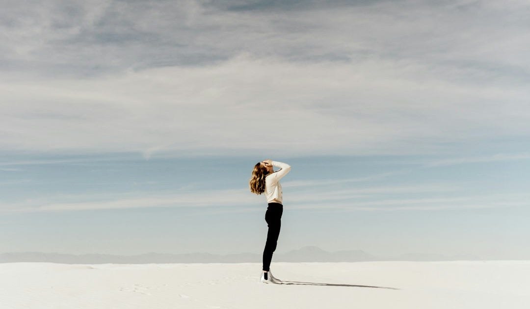woman looking up to the sky while standing on white sand