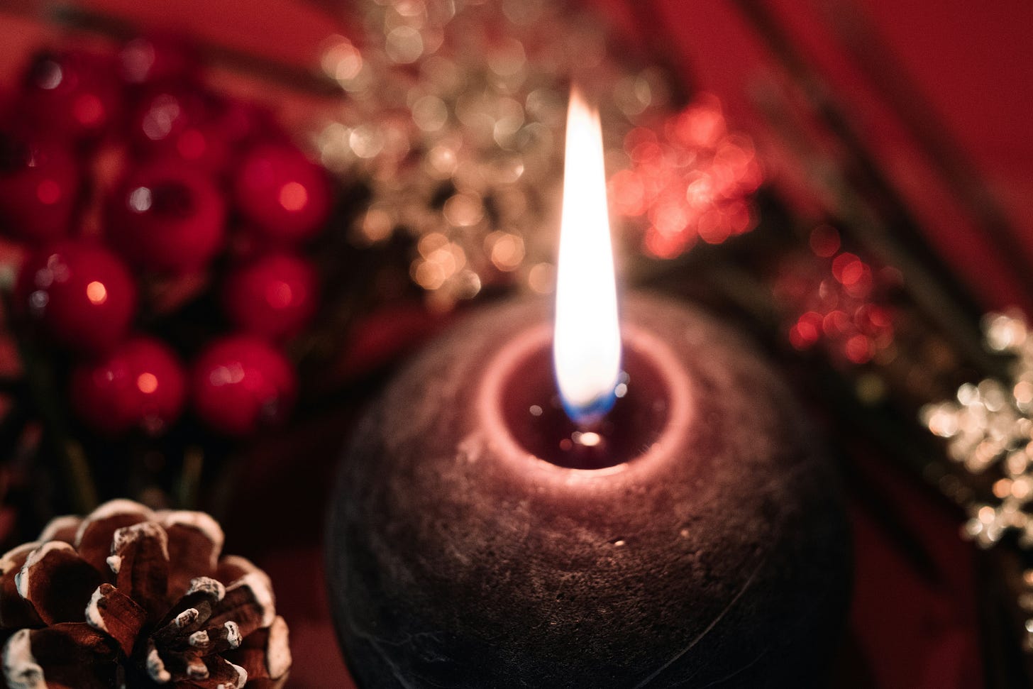A lit spherical candle sits in the center of lots of natural Christmas decorations including red berries and pinecones.