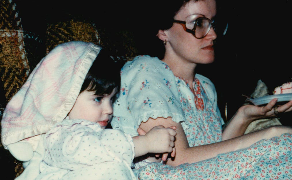 A little girl sitting on a couch next to her mom.