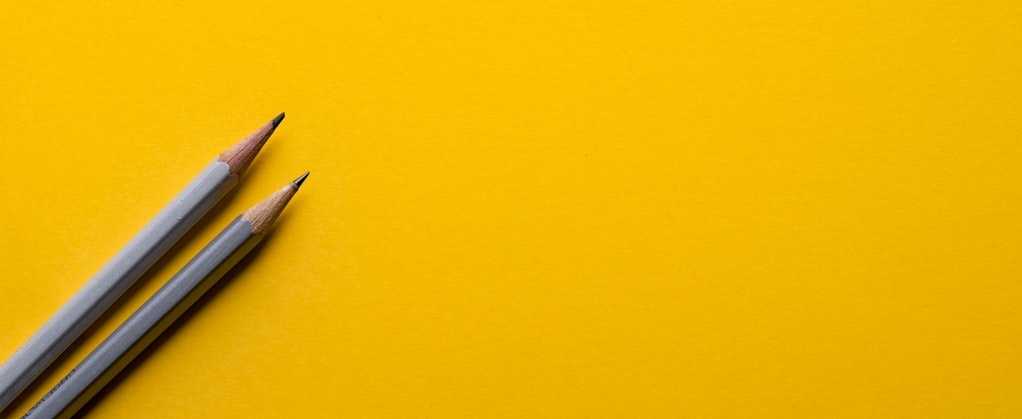 two gray pencils on yellow surface