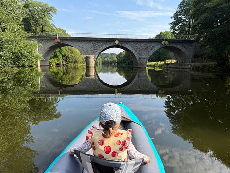 A grid of six summer photos. Top row: a boy kicking a soccer ball in a tree-lined field; a young girl paddling a small inflatable kayak on a river beneath a stone arched bridge; a girl in a pink fairy dress walking a sun-dappled forest path. Bottom row: a girl sitting on a leafy forest slope doing a beading craft; a child rowing a small boat on a calm green river; a boy and girl painting with watercolors at a table set with brushes and a star-patterned cloth.