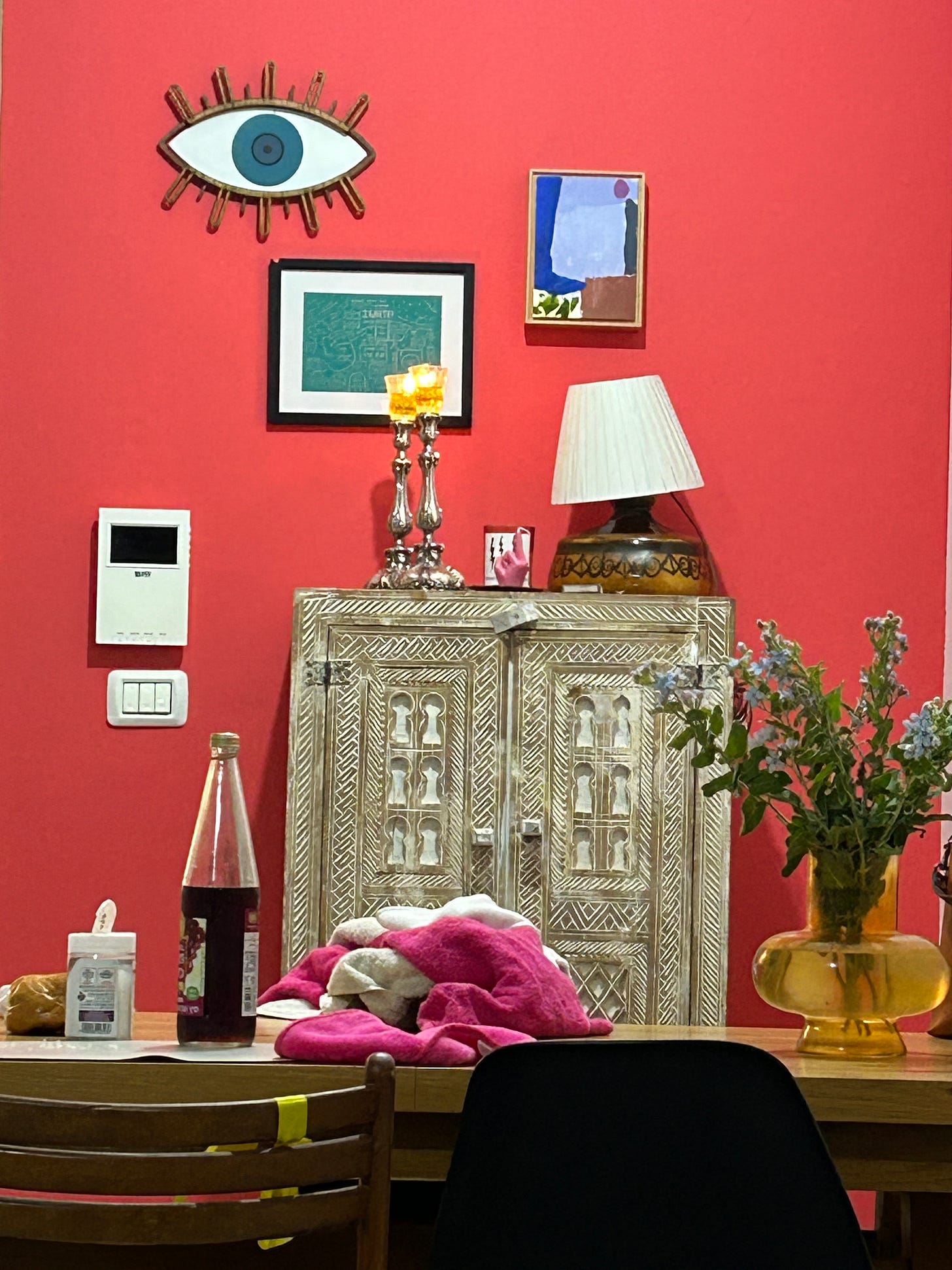 coral paint wall with art: wyw mask, small abstract painting, small map drawing, vintage lamp, all above a Moroccan inlaid cabinet