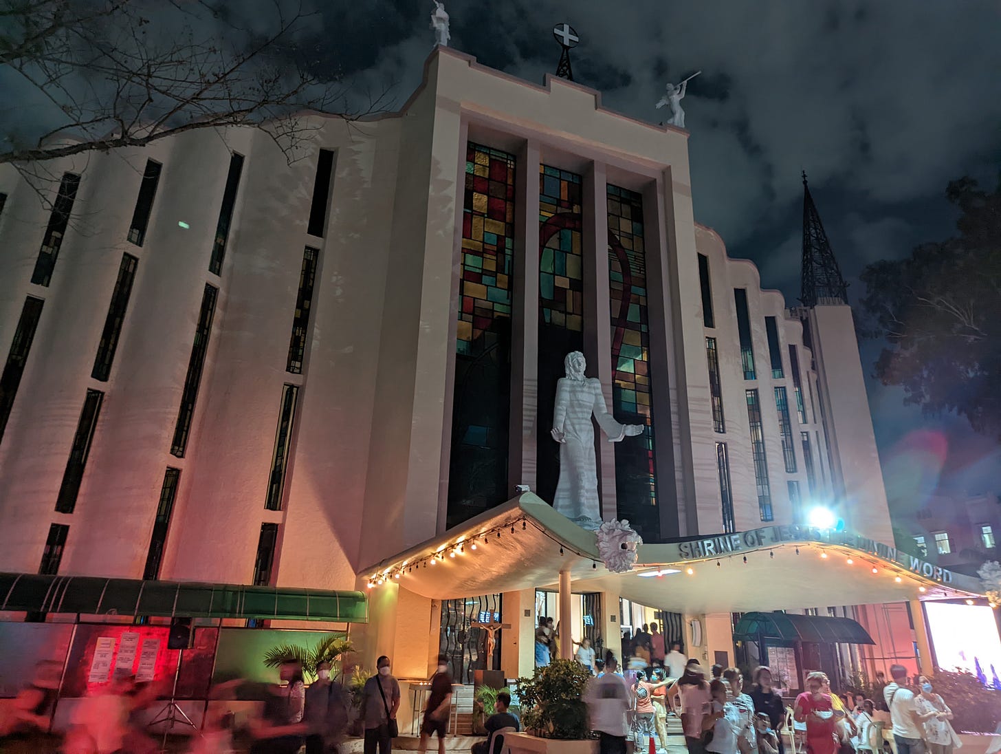 The dim-lit facade and main entrance of Jesus the Divine Word Church showing the many people entering and exiting