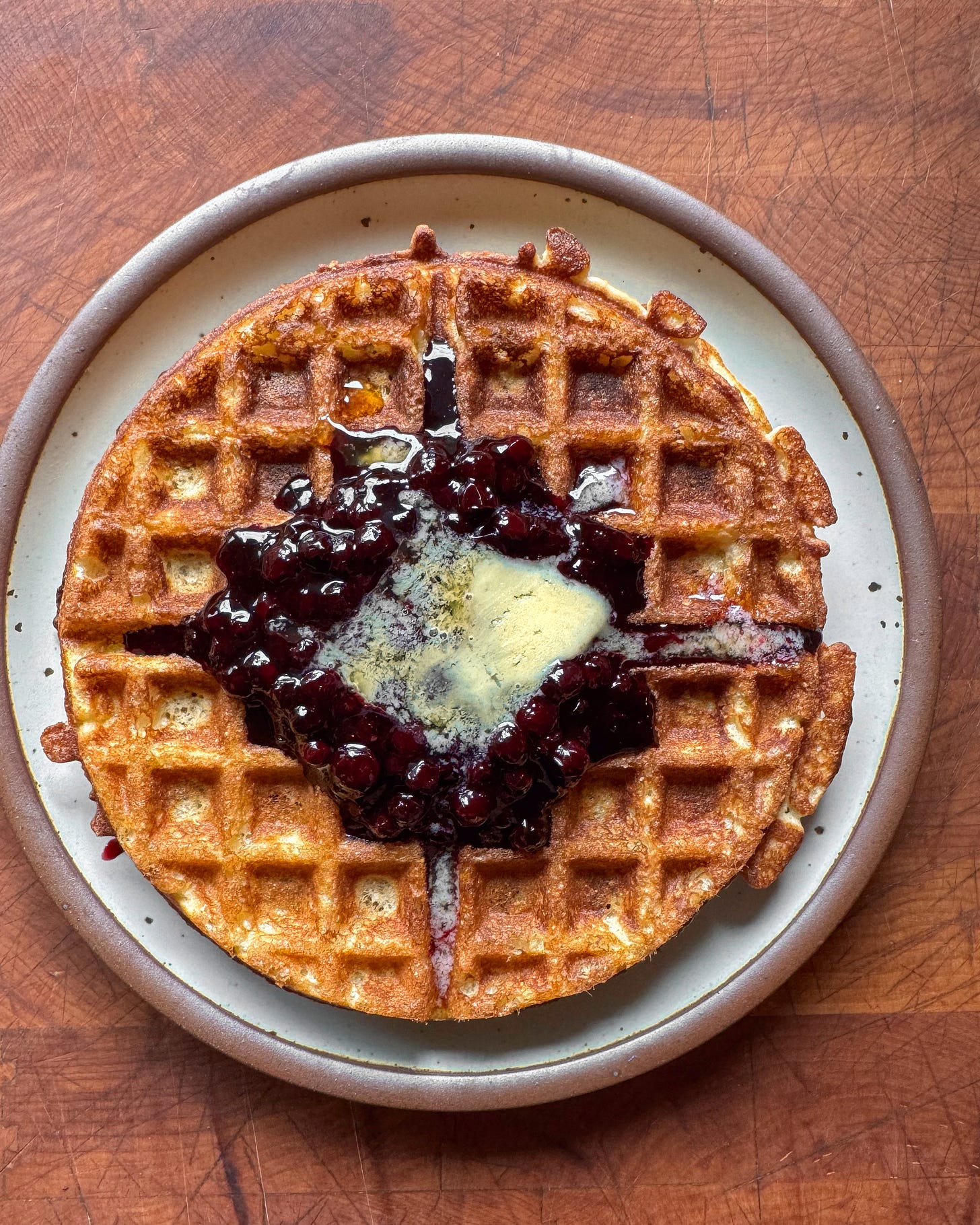 A golden brown cornmeal waffle topped with blueberry compote (a thick blueberry sauce) and a pat of butter that is melting