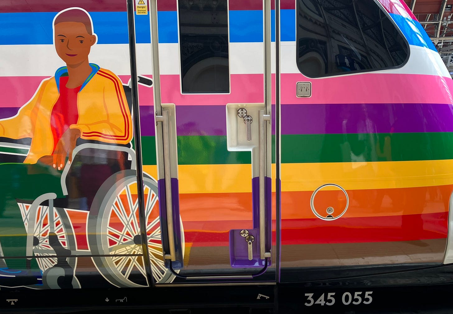 Top of the rainbow train, illustration of a black teenager in a hospital-like wheelchair with a yellow sports jacket, red t-shirt and green trousers, he sits very passively