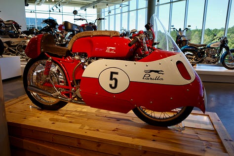 Barber Vintage Motorsports Museum Sign; vintage motorcycles on display; Jessica with her hair in two braids in one of the areas of the bike museum;dozens of bikes stacked on a very tall display; King Kenny Roberts wearing a cowboy hat and sitting on a yellow bike