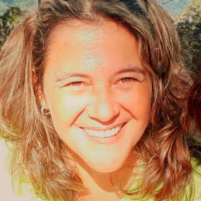 Retrato em close de uma mulher sorrindo diretamente para a câmera, com cabelos castanhos ondulados na altura dos ombros. Retrato em close de uma mulher sorrindo diretamente para a câmera, com cabelos castanhos ondulados na altura dos ombros.