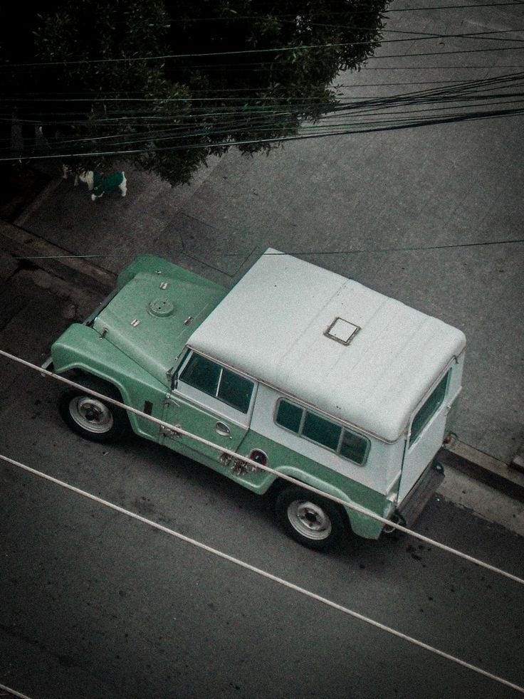 This may contain: an old green and white truck parked on the side of the road next to a tree