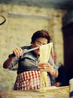 This may contain: a woman in an apron is using a knife to cut noodles