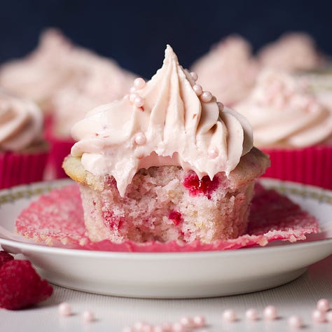 A raspberry cupcake on a plate, a slice of strawberry cream pie, and a slice of peach coffee cake.