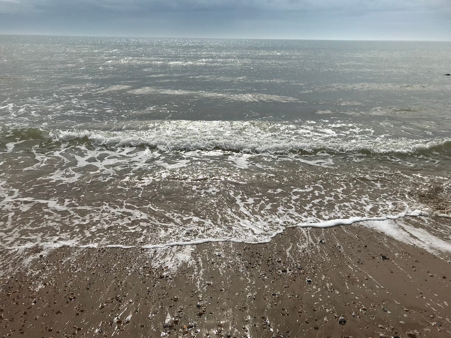 the sea from the shore, with sunlight dancing in the distance to the horizon and shallow lace edges lapping at the sand.