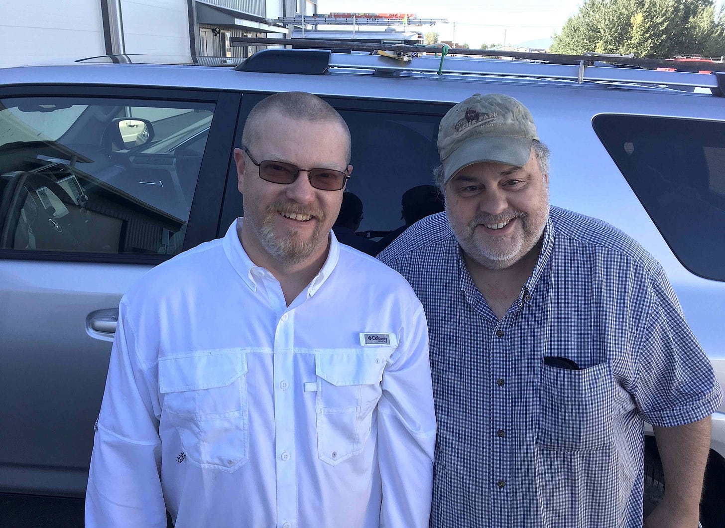 two men smiling next to a car