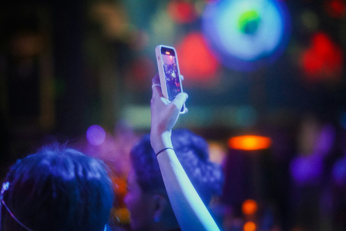 A person holding up their smartphone to film a performance in a venue with colourful lights. A person holding up their smartphone to film a performance in a venue with colourful lights.
