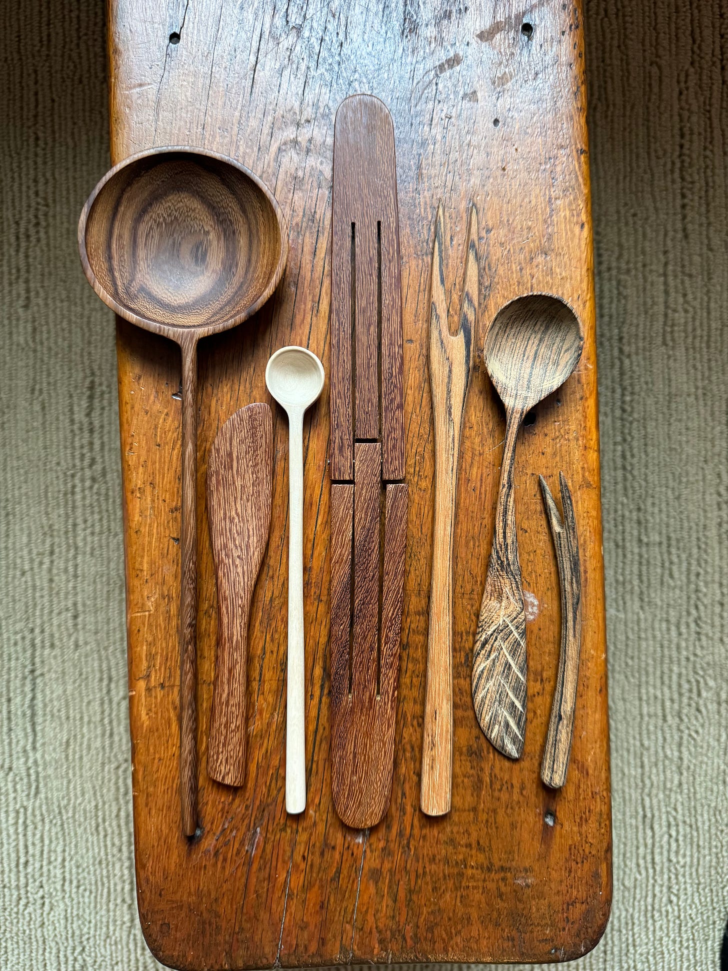 A set of carved wooden serving utensils on a wooden bench.