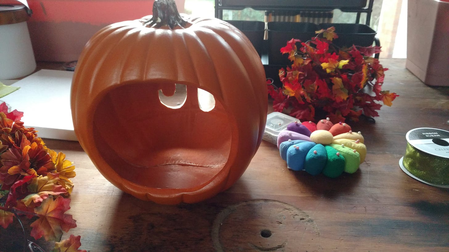 A craft pumpkin with an open back sits on a workbench. Crafting materials surround it.