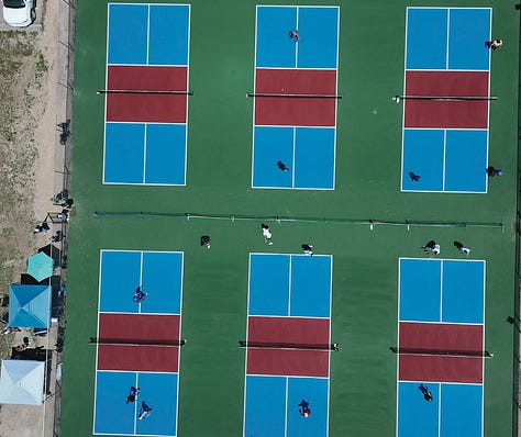 six pickleball courts, players in position, holding their paddles 