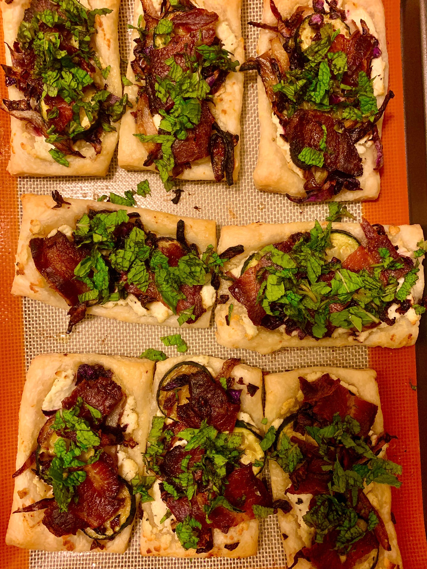Top view of puff pastry topped with cheese, vegetables, bacon, and herbs on a Silpat liner