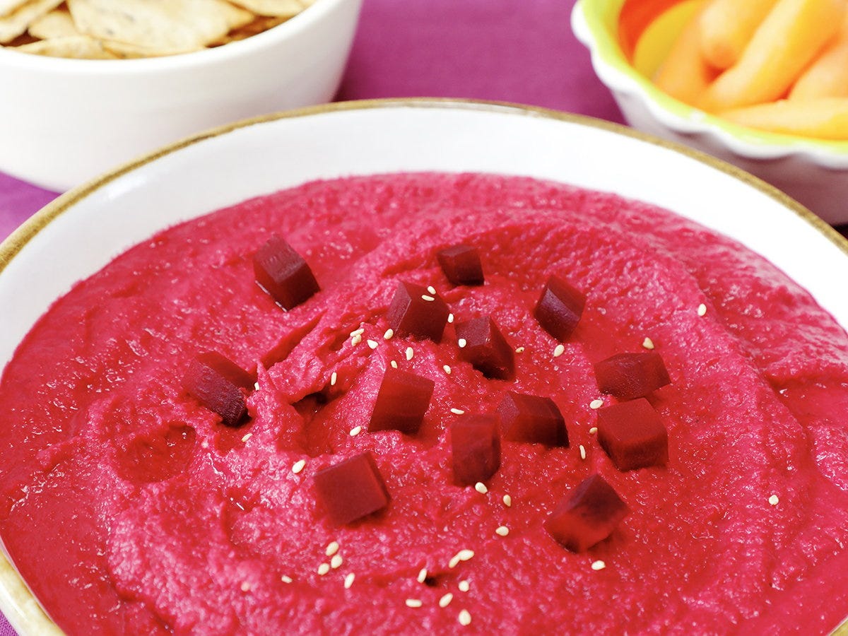 Closeup of bowl of red beet hummus sprinkled with beet cubes and sesame seeds