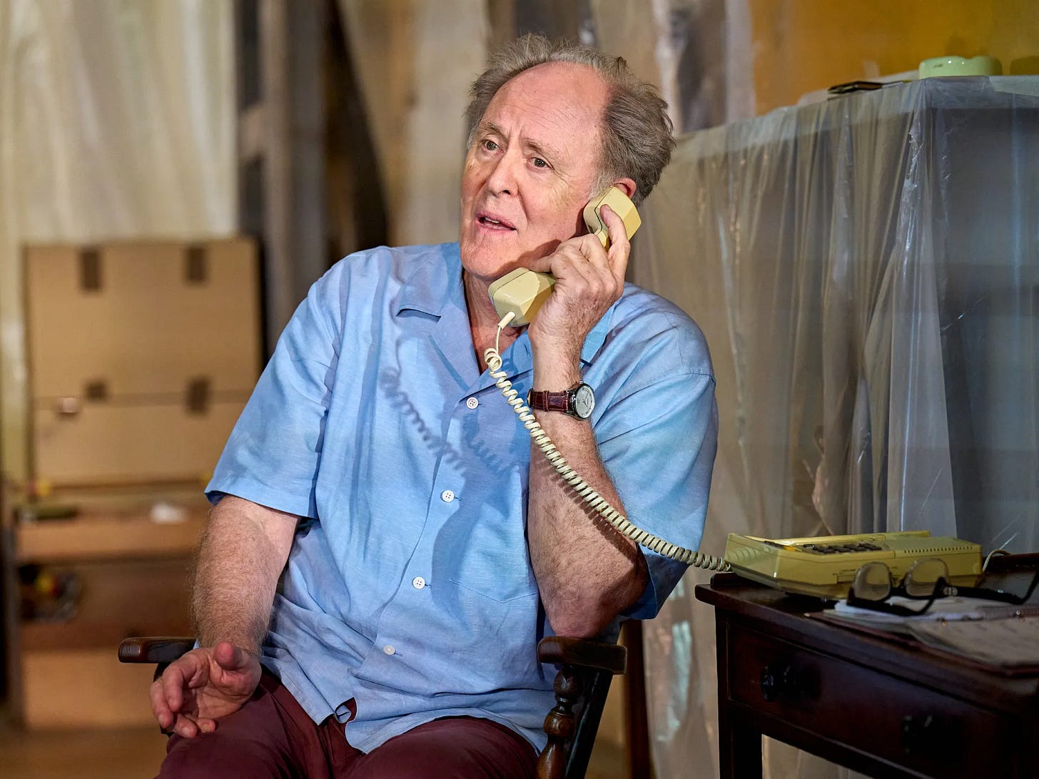 John Lithgow, as Roald Dahl, sitting at his desk and talking on the telephone.