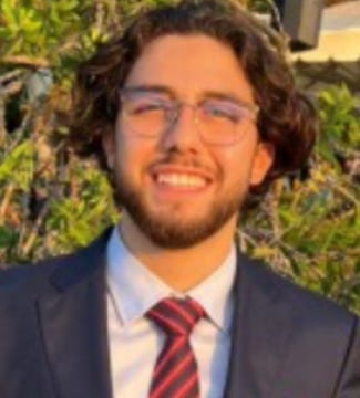 First image shows a young man with curly dark hair, wearing clear-framed glasses, a white dress shirt, red striped tie, and dark suit jacket, smiling slightly outdoors with green foliage and a blurred background. Second image depicts the same man with long dark wavy hair and beard, neutral expression, against a plain gray background resembling a mugshot or ID photo.