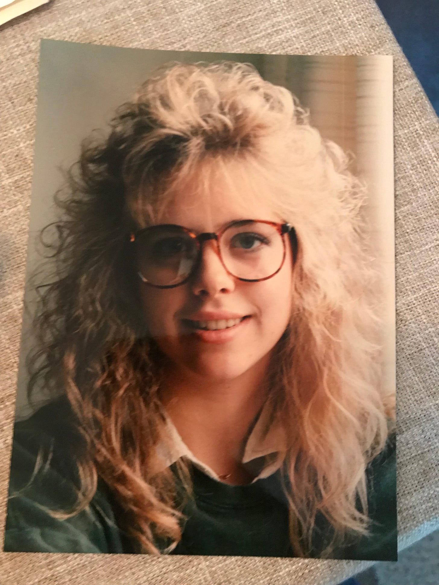 Picture of the author at 16 with fake big tortoise glasses and the spiral perm once it settled down- bangs tall and round and in their 80's glory!