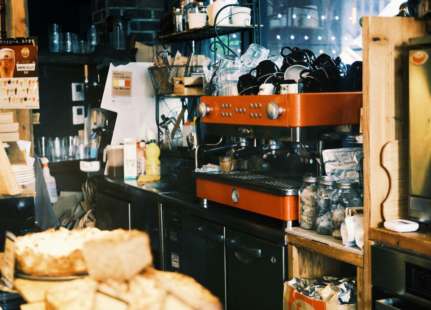 A cluttered café counter with an orange espresso machine, stacked cups, glass jars, and fresh bread in the foreground—the kind of local spot visitors remember long after they leave. A cluttered café counter with an orange espresso machine, stacked cups, glass jars, and fresh bread in the foreground—the kind of local spot visitors remember long after they leave.
