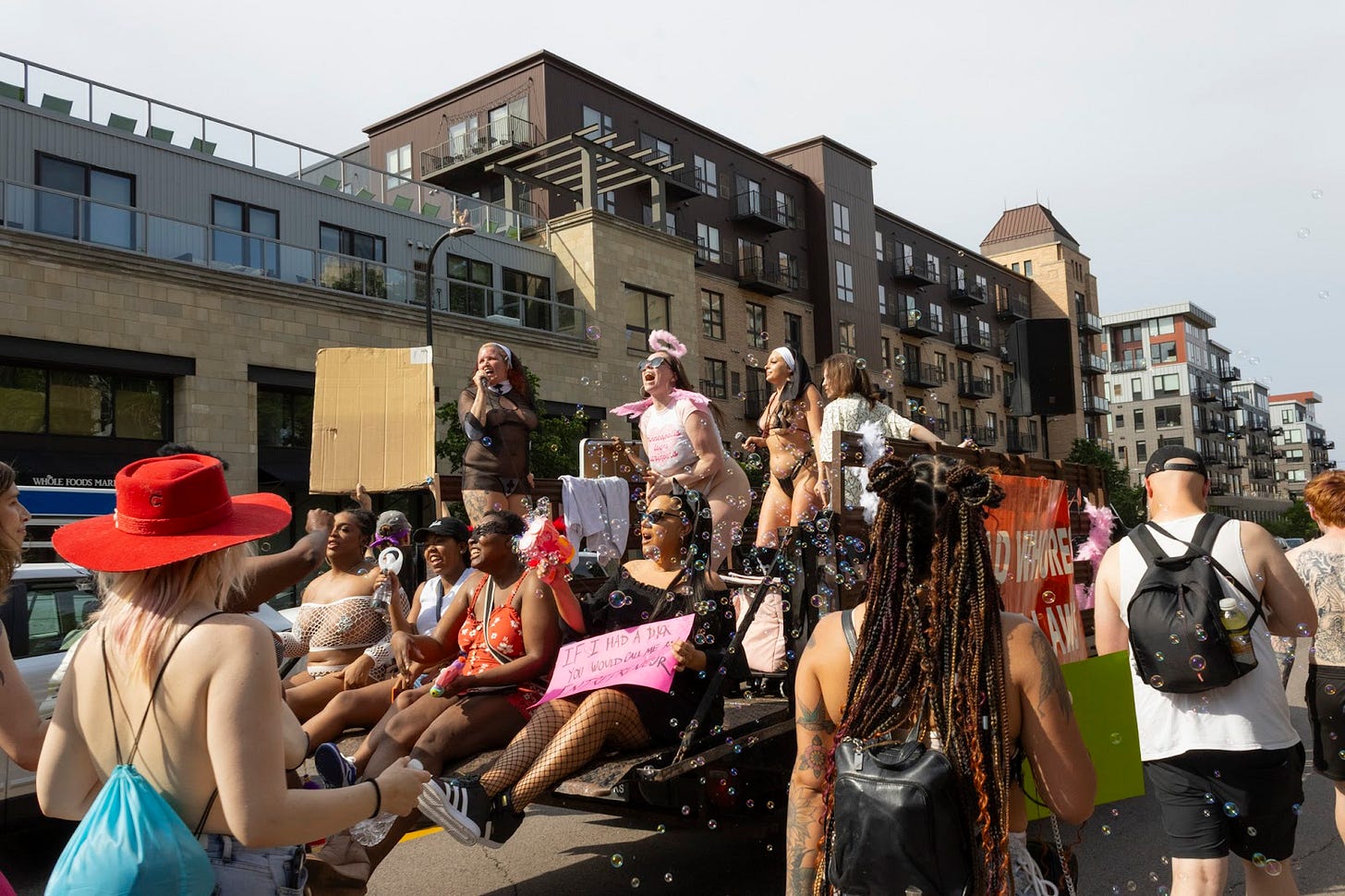 people wearing lingerie and mesh sit and stand on the back of a truck blowing bubbles as people parade past them people wearing lingerie and mesh sit and stand on the back of a truck blowing bubbles as people parade past them