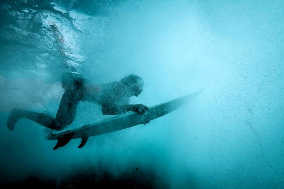 Surfer underwater with surfboard in blue ocean
