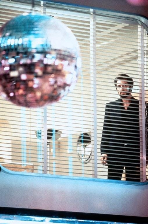 This may contain: a man standing in front of a mirror with a disco ball hanging from it's side