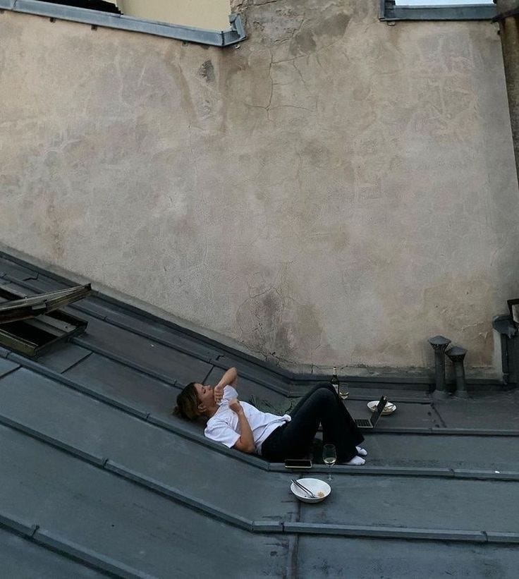 This may contain: a woman laying on top of a metal roof next to a building with two windows