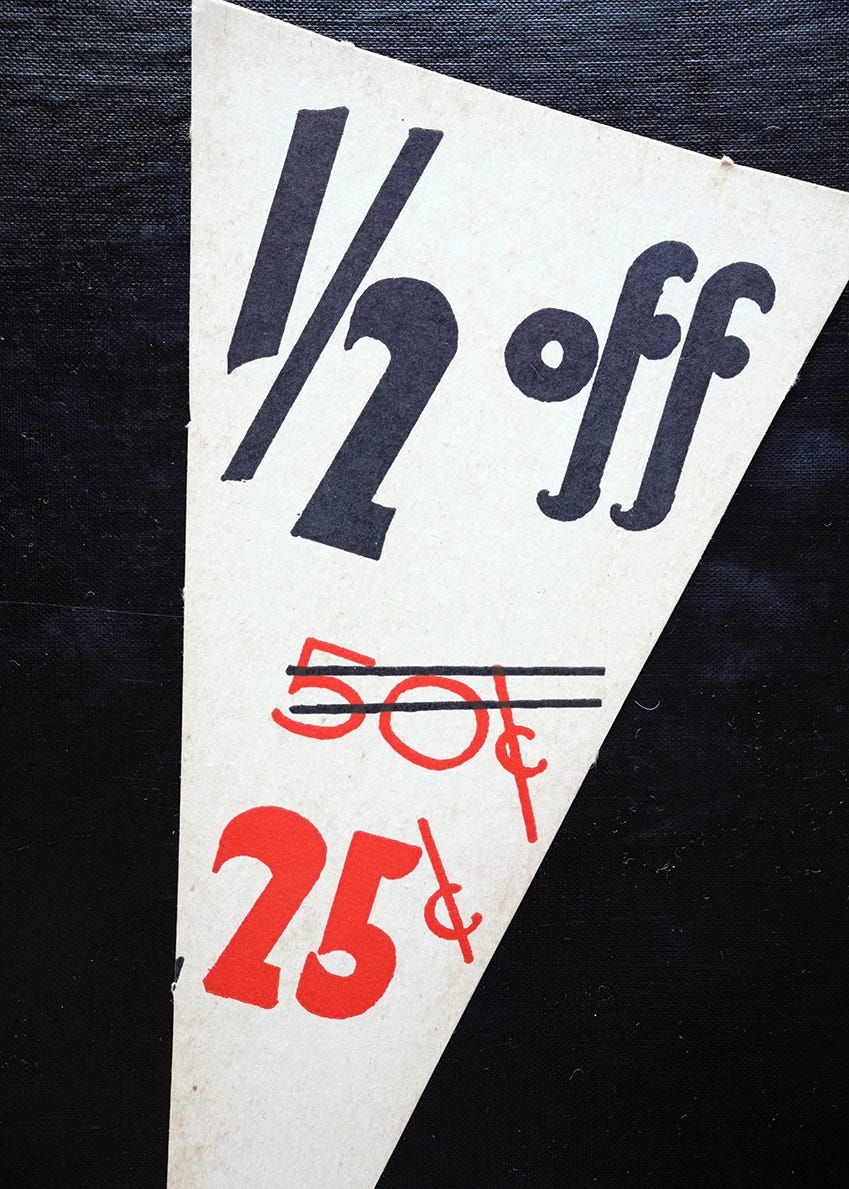 Vintage triangular retail price card reading '1/2 off' in bold black lettering, with the original price of 50¢ struck through in red and the sale price of 25¢ below it.