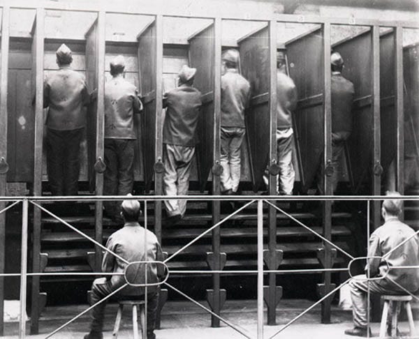 Black and white photograph of male prisoners walking a treadmill in individual partitioned stalls at Pentonville Prison.