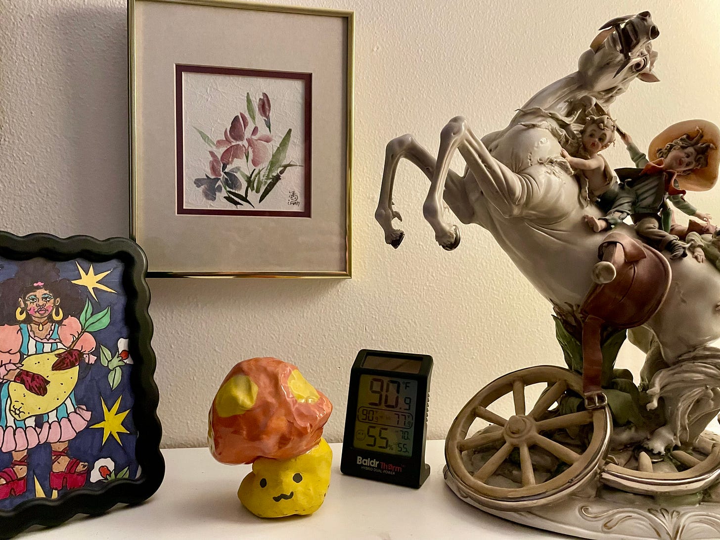 A collection of small artworks, including a rice paper print, marker illustration, simple mushroom sculpture, and an old-fashioned horse with kids dressed as cowboys riding it statue. There's also a thermometer reading 90 degrees Fahrenheit and 55% humidity. A collection of small artworks, including a rice paper print, marker illustration, simple mushroom sculpture, and an old-fashioned horse with kids dressed as cowboys riding it statue. There's also a thermometer reading 90 degrees Fahrenheit and 55% humidity.