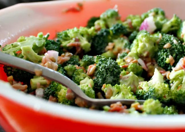 side view of a spoon scooping broccoli salad out of a red bowl