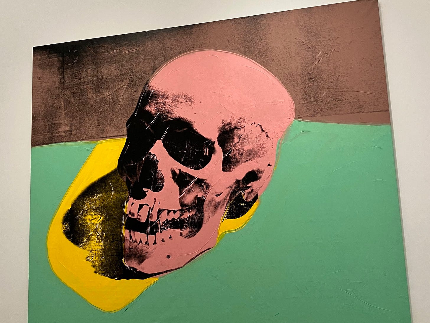 An Andy Warhol painting titled Skull. It contains a pink skull, a black shadow, against a yellow, green, and black background.
