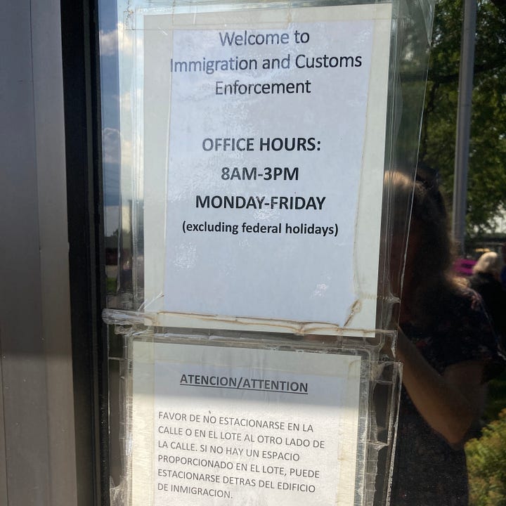 Homeland Security sign on brick building. Paper signs taped on a window reading "Welcome to Immigration and Customs Enforcement. OFFICE HOURS 8 am-3 pm MONDAY-FRIDAY excluding federal holidays and parking instructions in Spanish