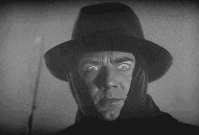 a black and white photo of a man wearing a fedora and gloves