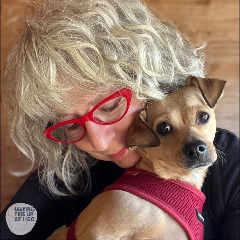 a woman wearing red glasses looks down at the golden chiweenie sitting on her lap