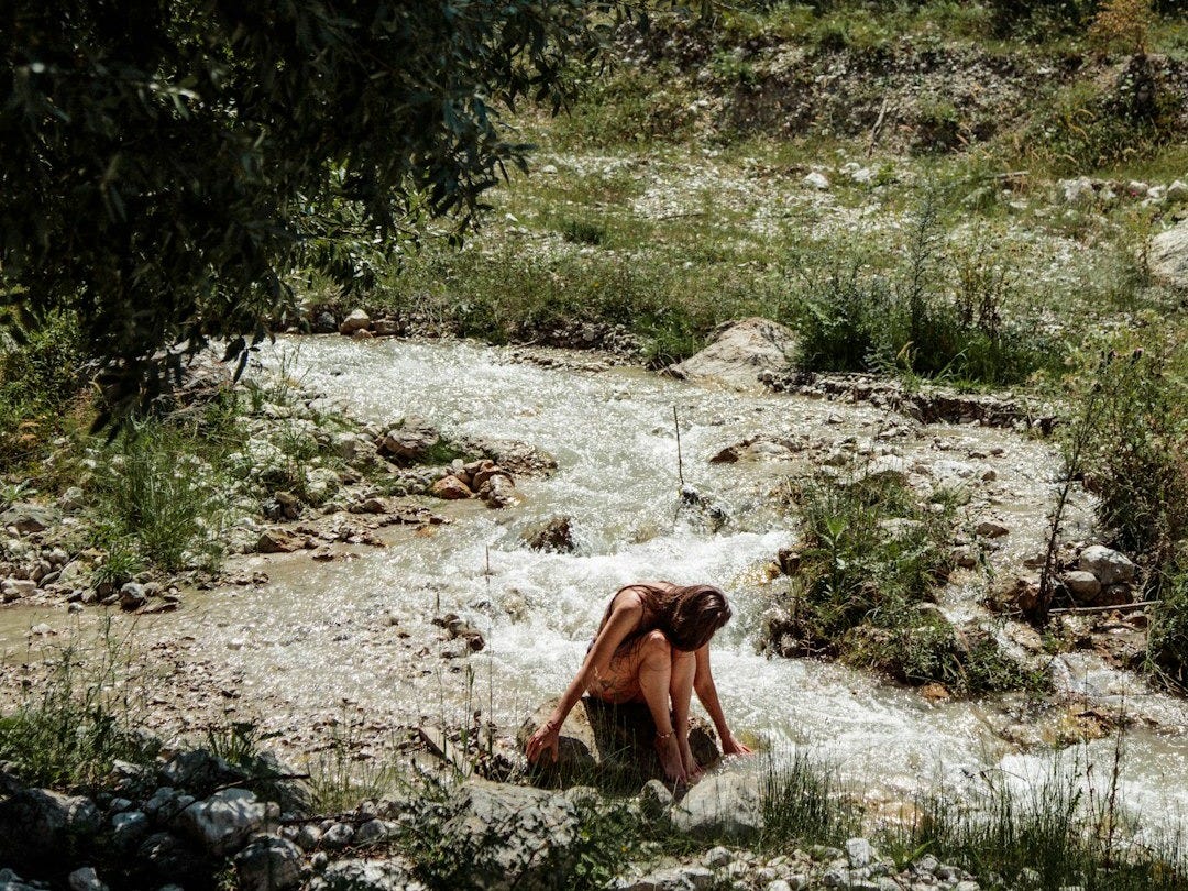 a woman sitting on the ground next to a river