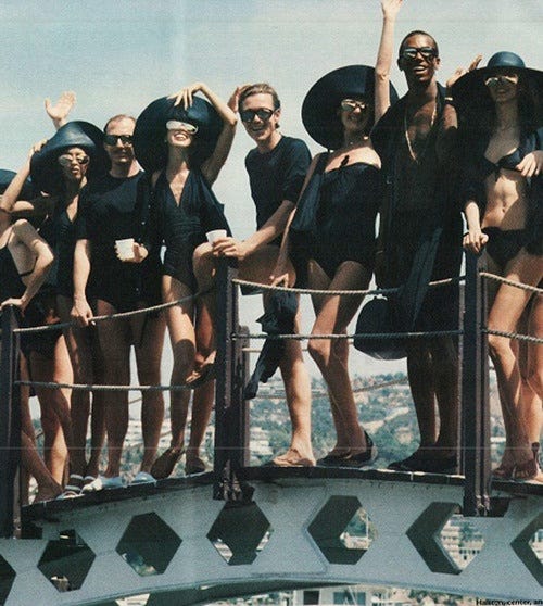 This may contain: a group of women standing on top of a bridge wearing black bathing suits and hats
