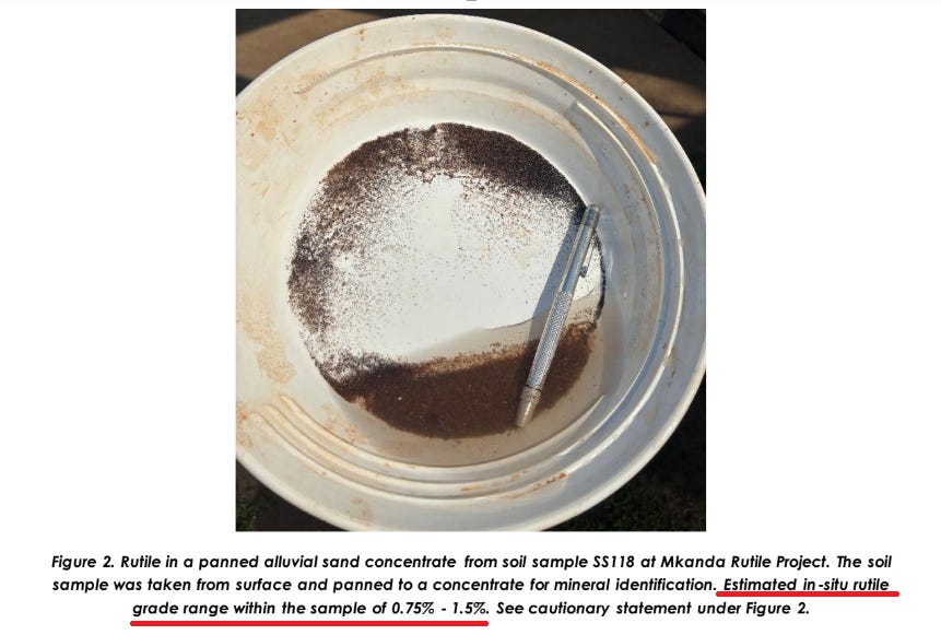 White pan with dark mineral concentrate and metal tool, showing rutile sample from Mkanda Rutile Project.