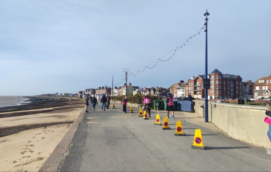 Cones mark the finish line on the promenade, under blue skies, with a yellow sandy beach to the side.
