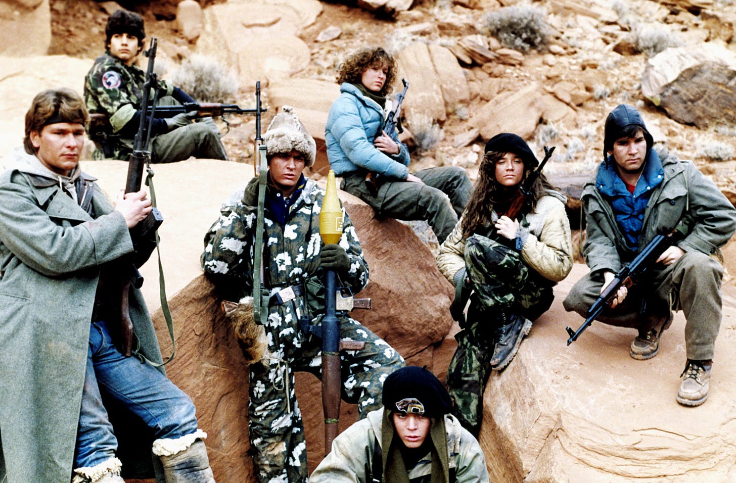 5 high school boys, two girls, with rifles and camouflage and winter hats and coats, pose on rocks