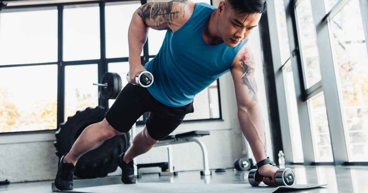 concentrated young sportsman exercising with dumbbells in gym on sport mat concentrated young sportsman exercising with dumbbells in gym on sport mat
