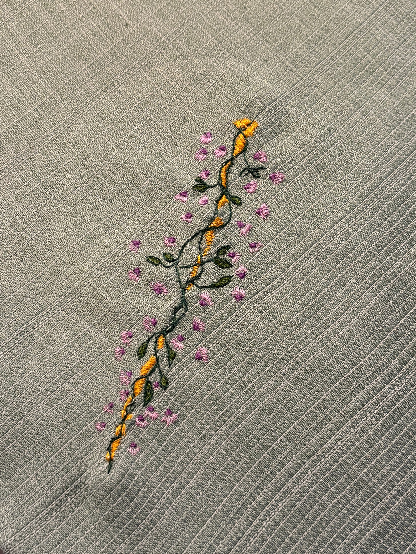 Close up of an embroidered vine surrounded by pink and purple flowers on a green background